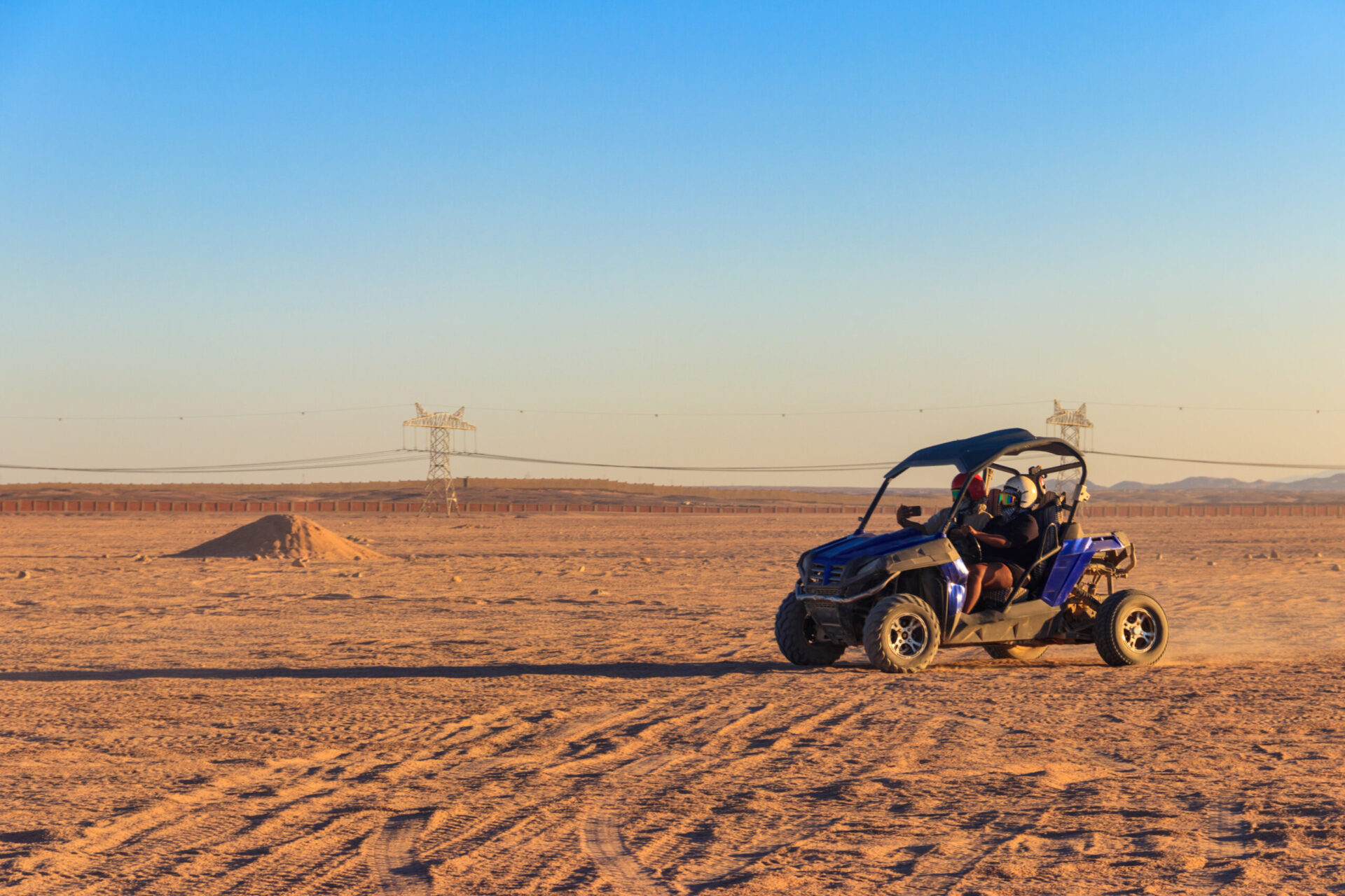 Vehículo todoterreno azul circulando por un desierto amplio bajo un cielo despejado.