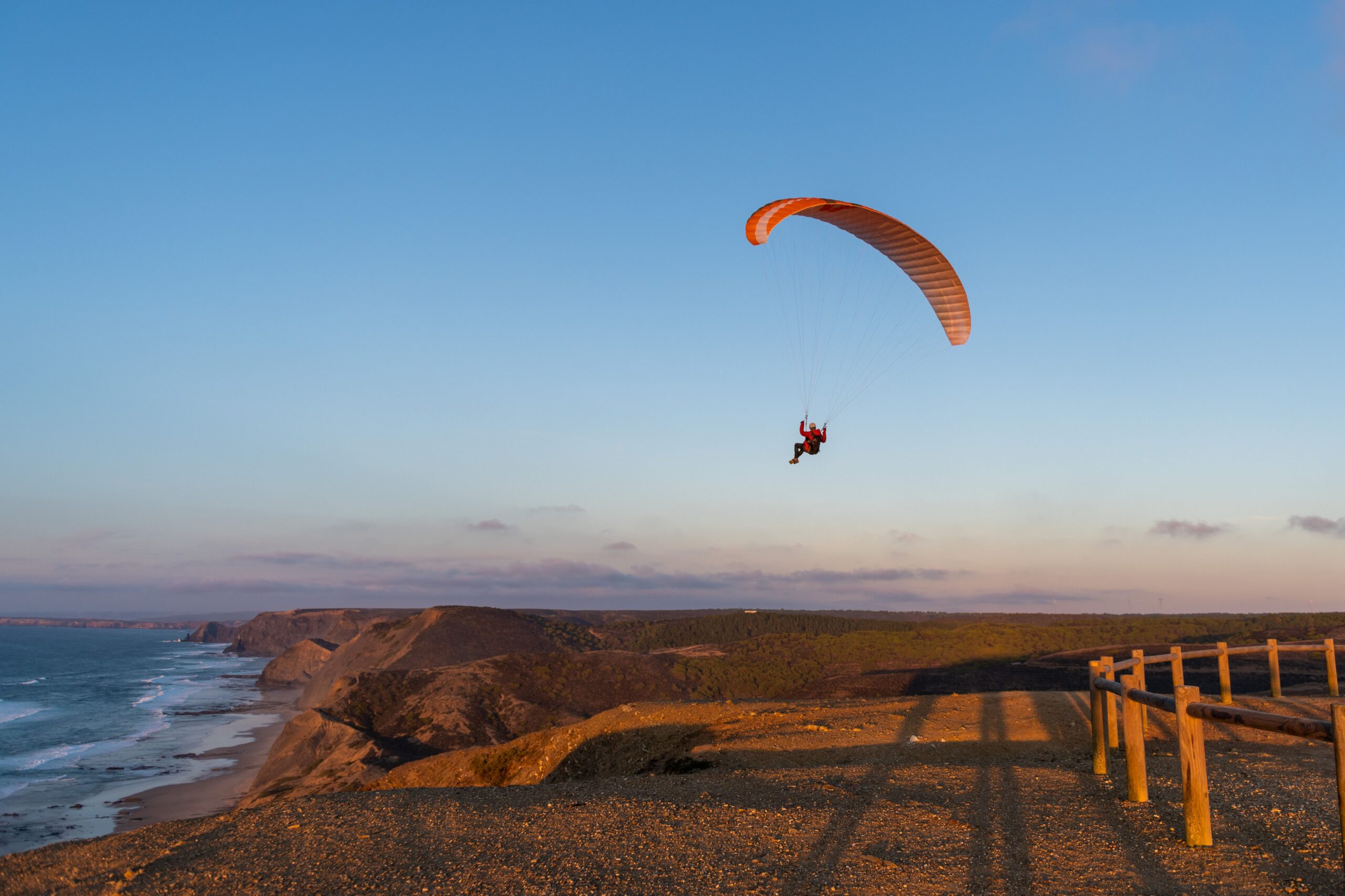 Persona volando en parapente sobre la costa al atardecer