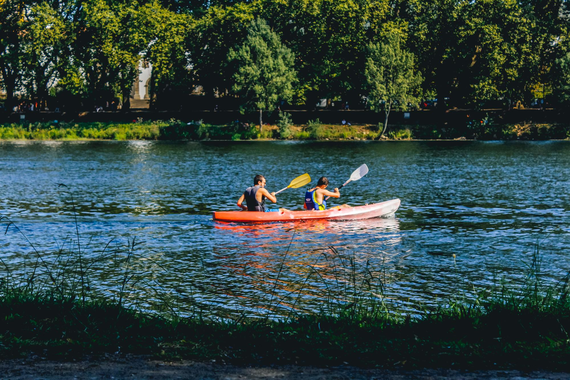 Dos personas practicando kayak en un río tranquilo rodeado de naturaleza