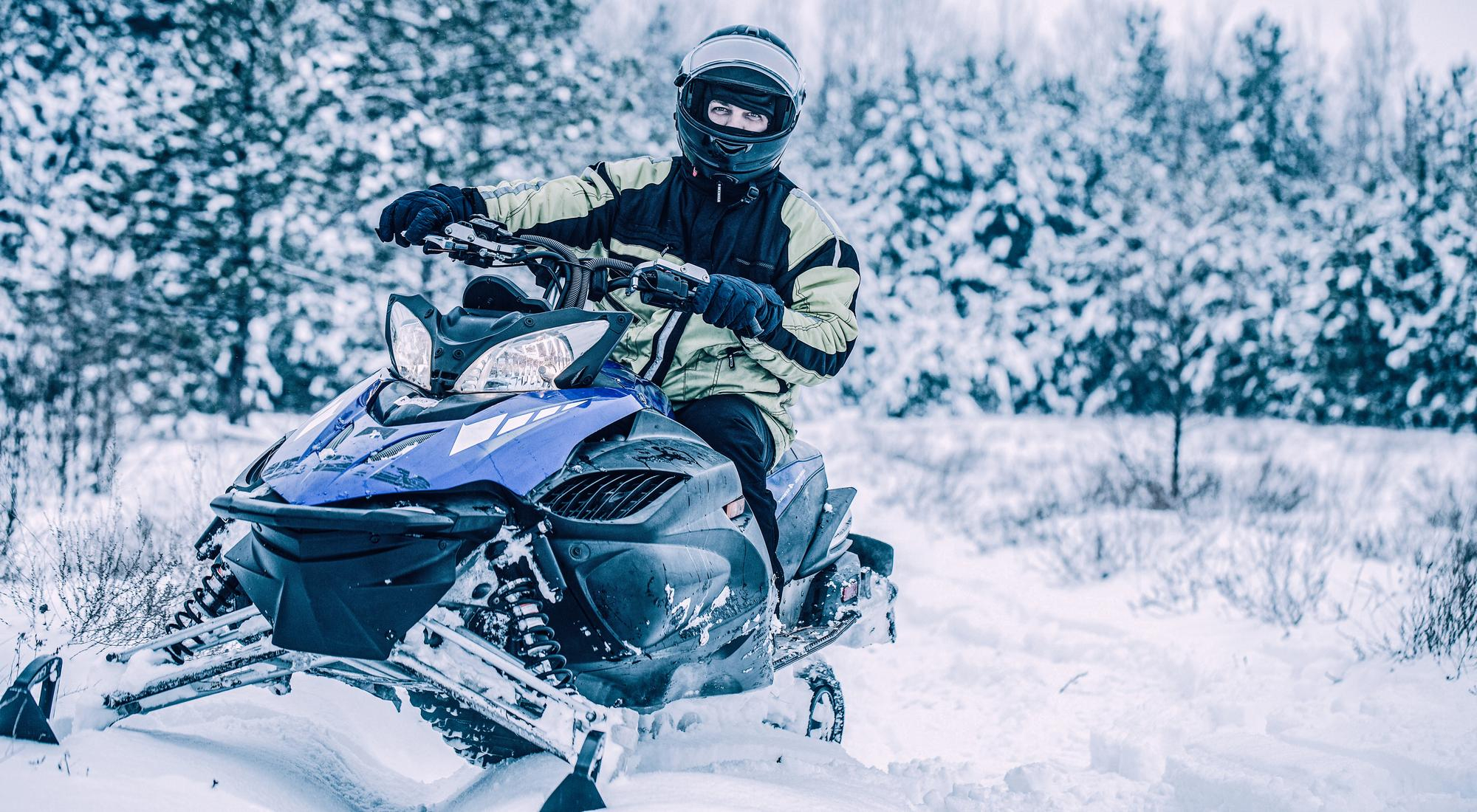 Persona equipada con casco y ropa térmica conduciendo una moto de nieve sobre un terreno nevado en invierno.