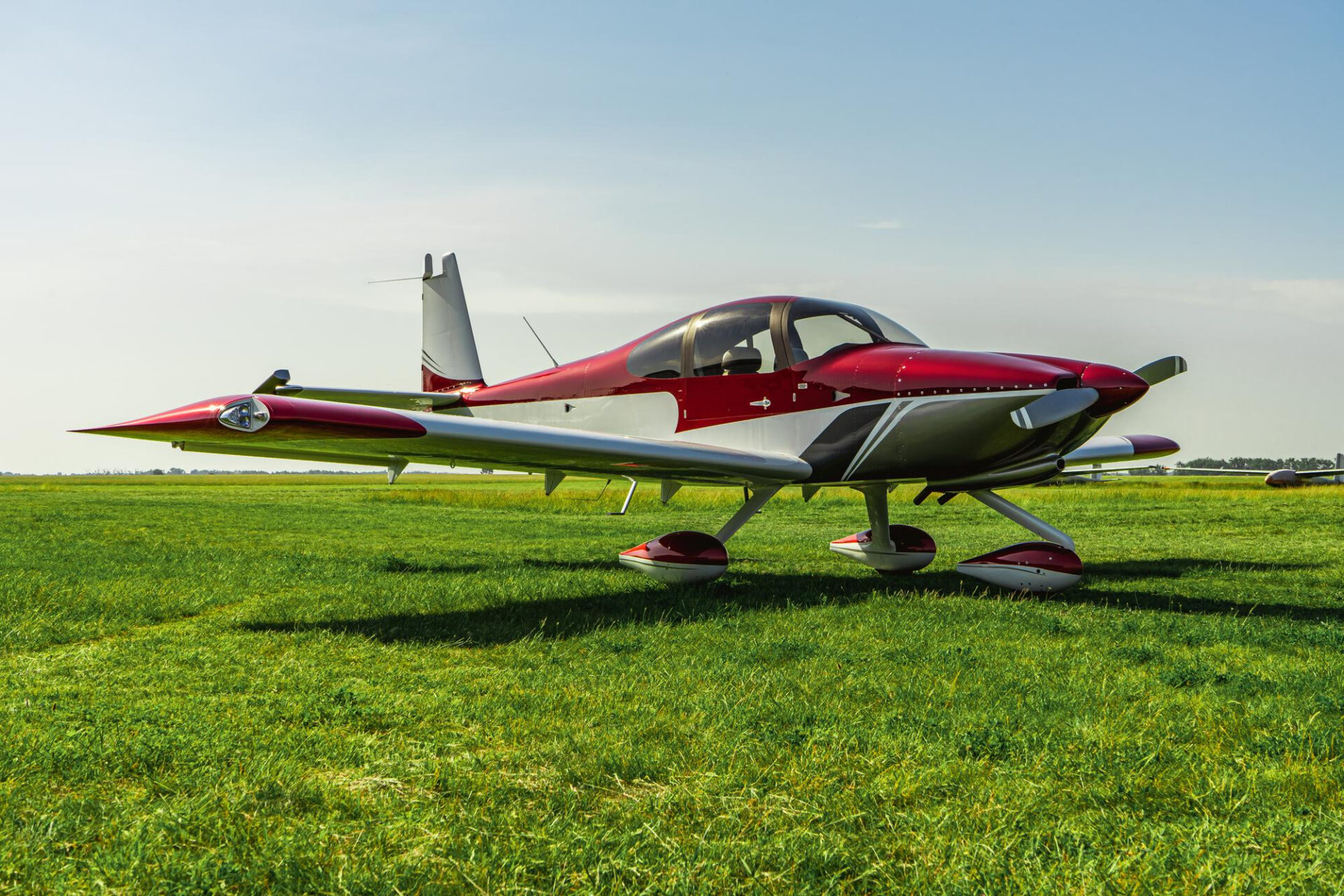 Avión ligero deportivo estacionado sobre el césped en un aeródromo al aire libre.