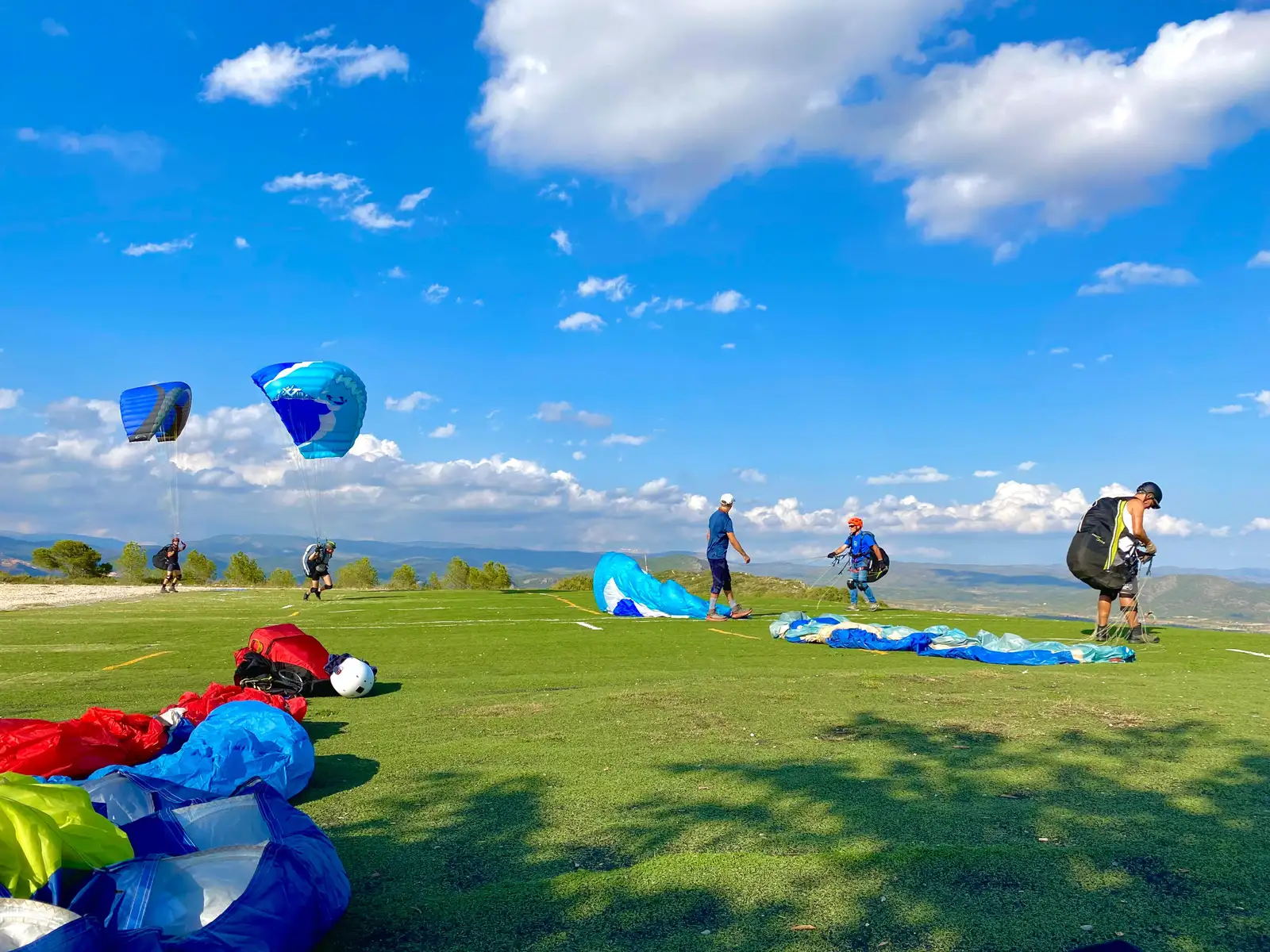 Personas preparando el despegue en parapente en una colina con cielo azul y paisaje natural