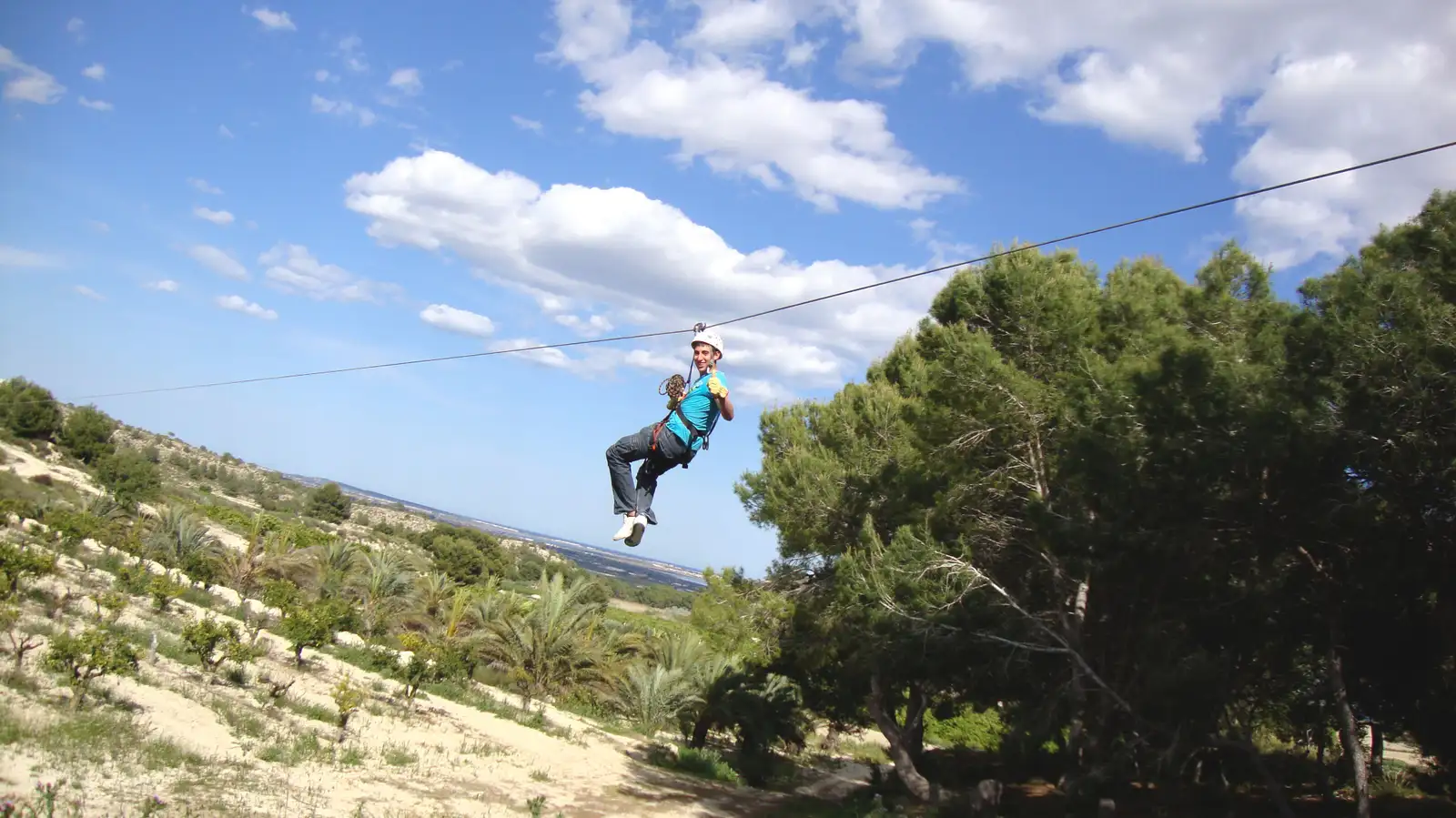Persona deslizándose por una tirolina sobre un paisaje natural con árboles y cielo despejado
