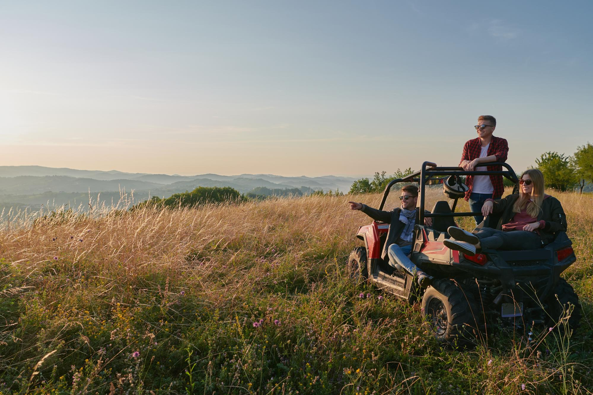 Un grupo de amigos disfrutando del paisaje durante un tour en buggy en una colina cubierta de hierba al atardecer.