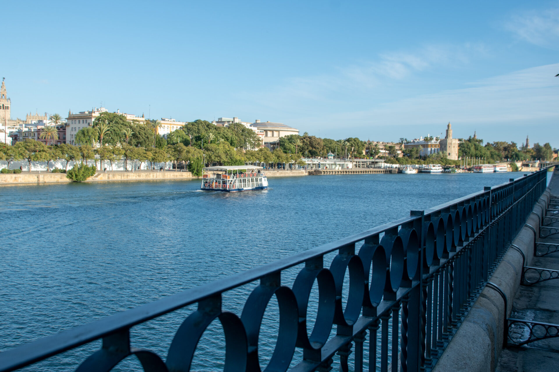 Barco turístico navegando por el río Guadalquivir en Sevilla con la Torre del Oro al fondo y el paseo fluvial