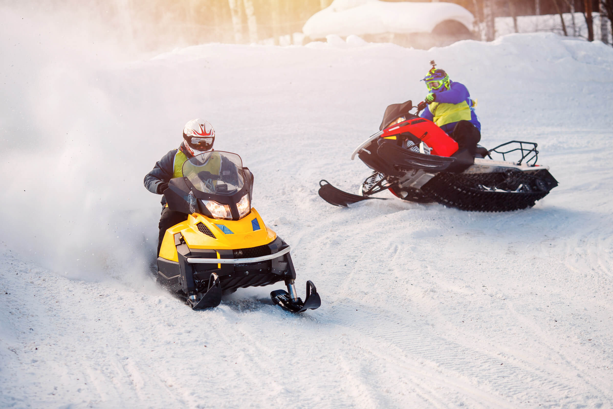 Dos personas conduciendo motos de nieve, una amarilla y otra roja, sobre una pista nevada durante un día de invierno