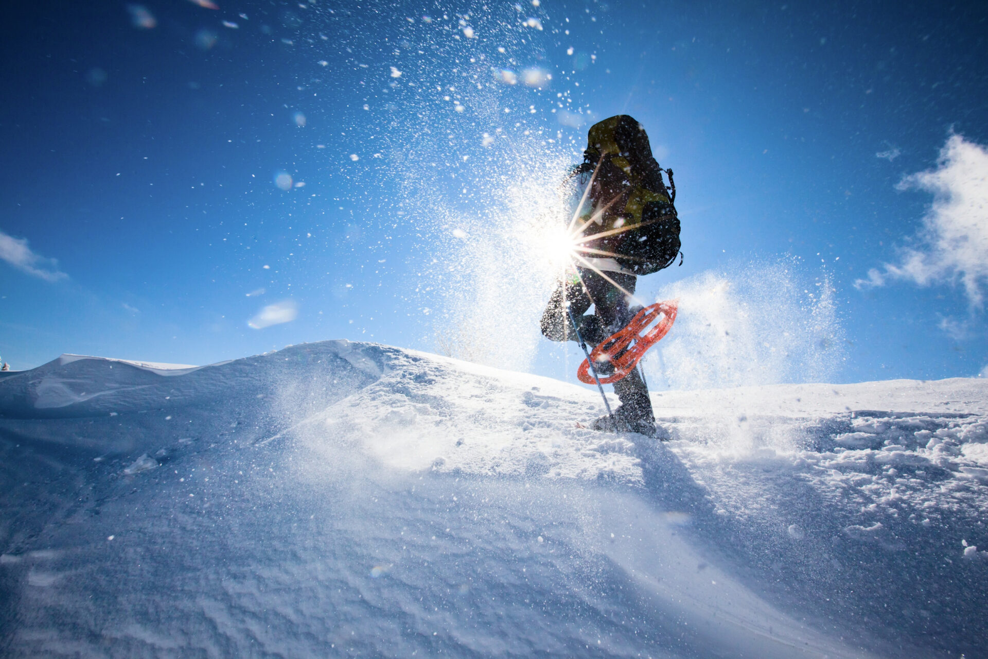 Hombre practicando senderismo invernal con raquetas de nieve entre montañas nevadas y cielo azul