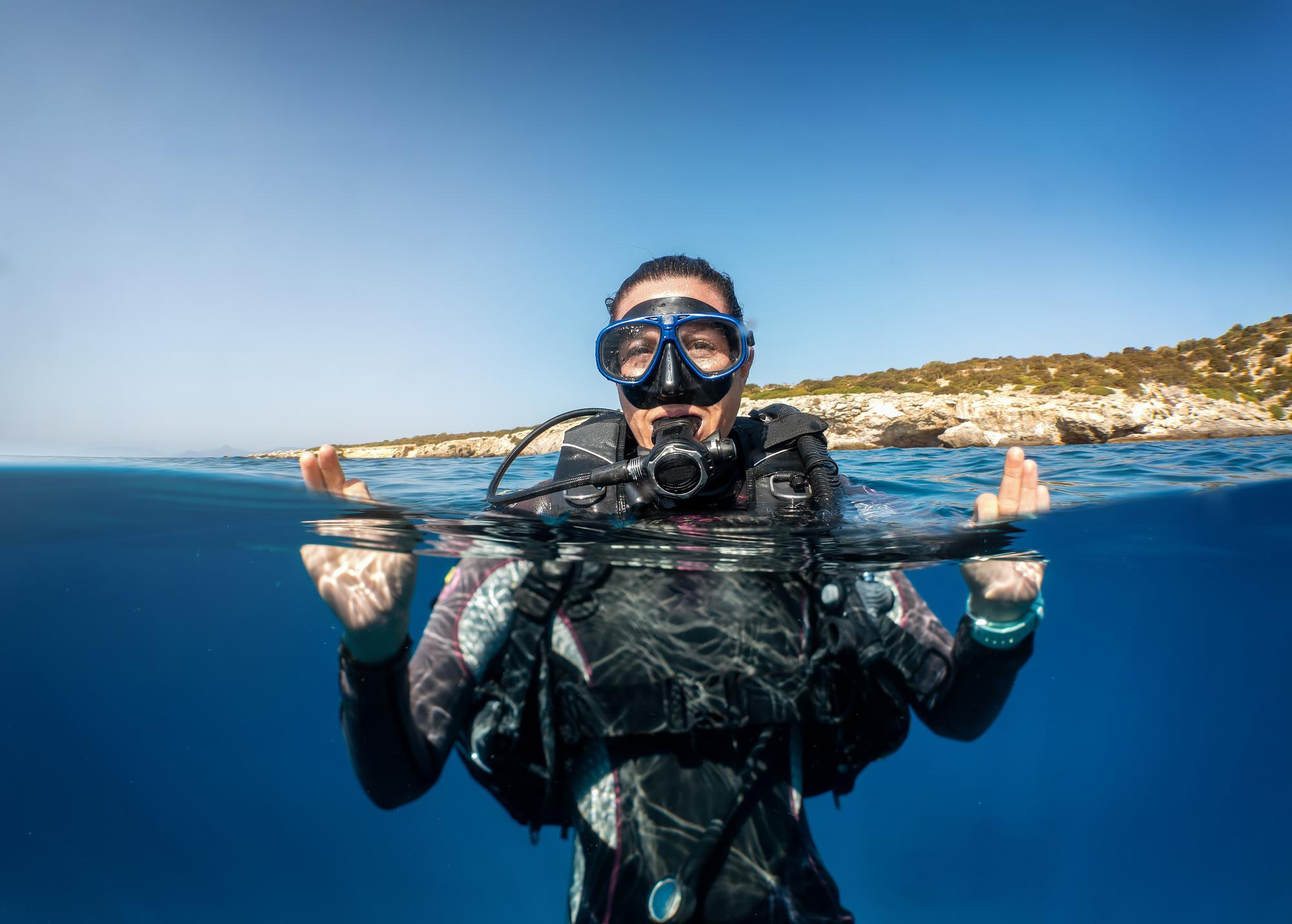 Mujer con equipo completo de buceo flotando en la superficie del mar azul cristalino durante un día soleado.