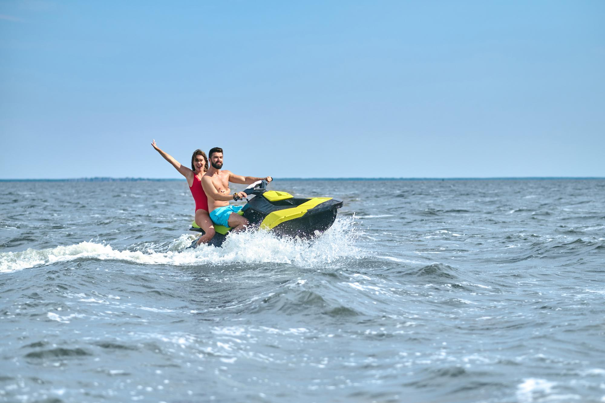 Pareja divirtiéndose y saludando mientras recorre el mar en una moto de agua