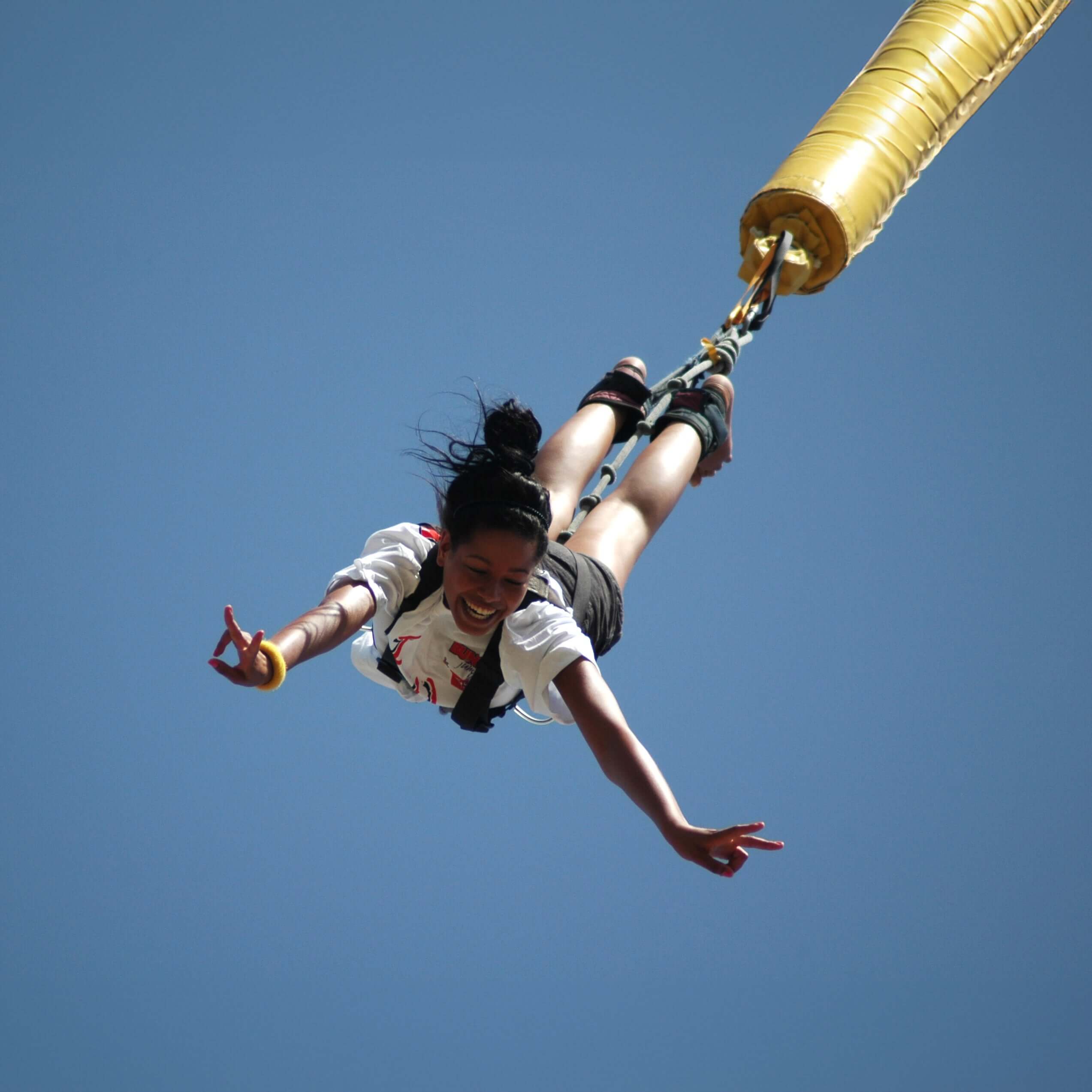Persona en pleno salto de puenting suspendida en el aire con la cuerda elástica tensada y el cielo azul de fondo