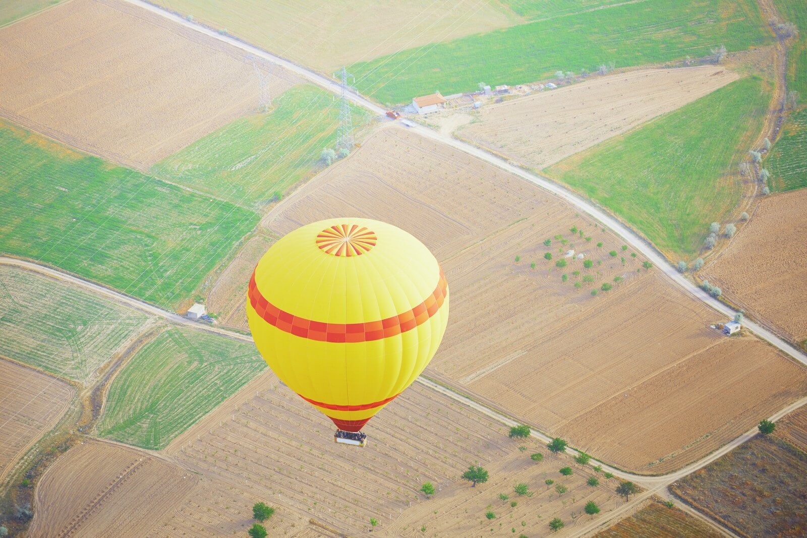 Globo aerostatico amarillo volando sobre campos agricolas con vista aerea del paisaje rural