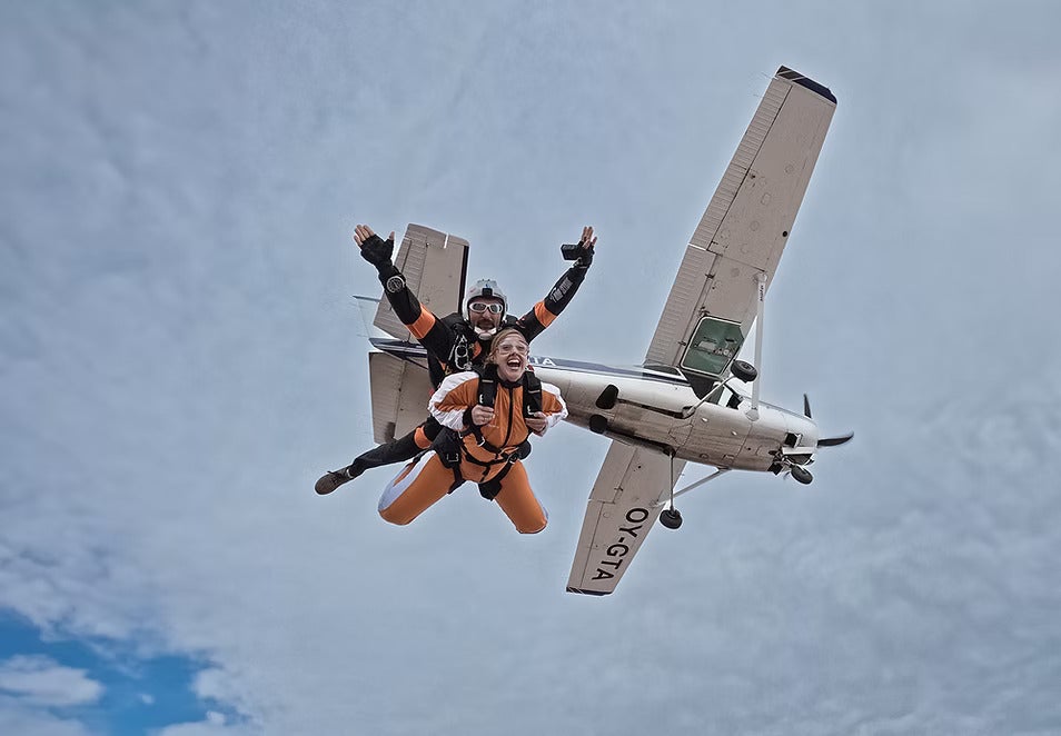 Una mujer y su instructor realizando un salto en paracaídas tándem justo después de saltar de una avioneta blanca en pleno vuelo