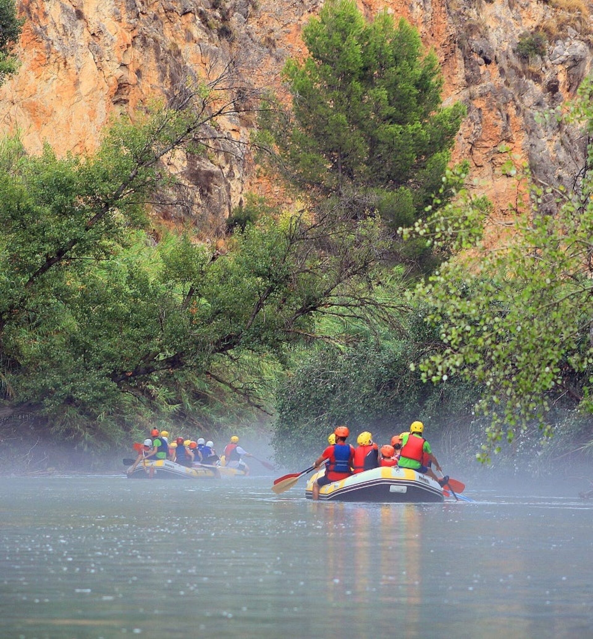 Grupo de personas haciendo rafting en un río rodeado de vegetación y paredes rocosas, una actividad de aventura complementaria al puenting