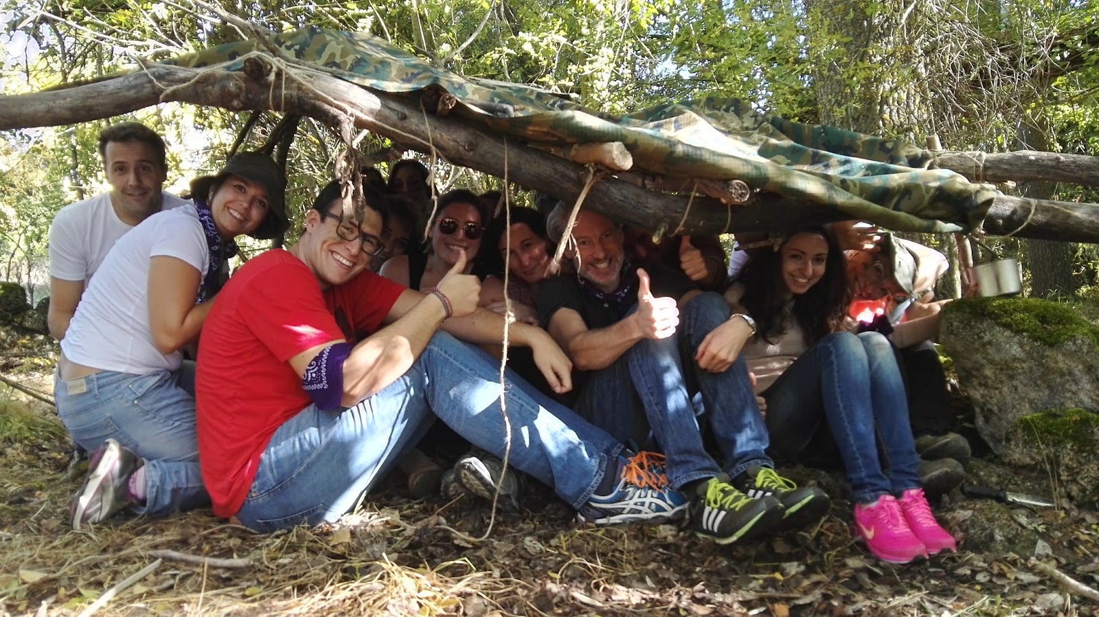 Grupo de compañeros posando dentro de un refugio construido con ramas en el bosque durante un curso de supervivencia