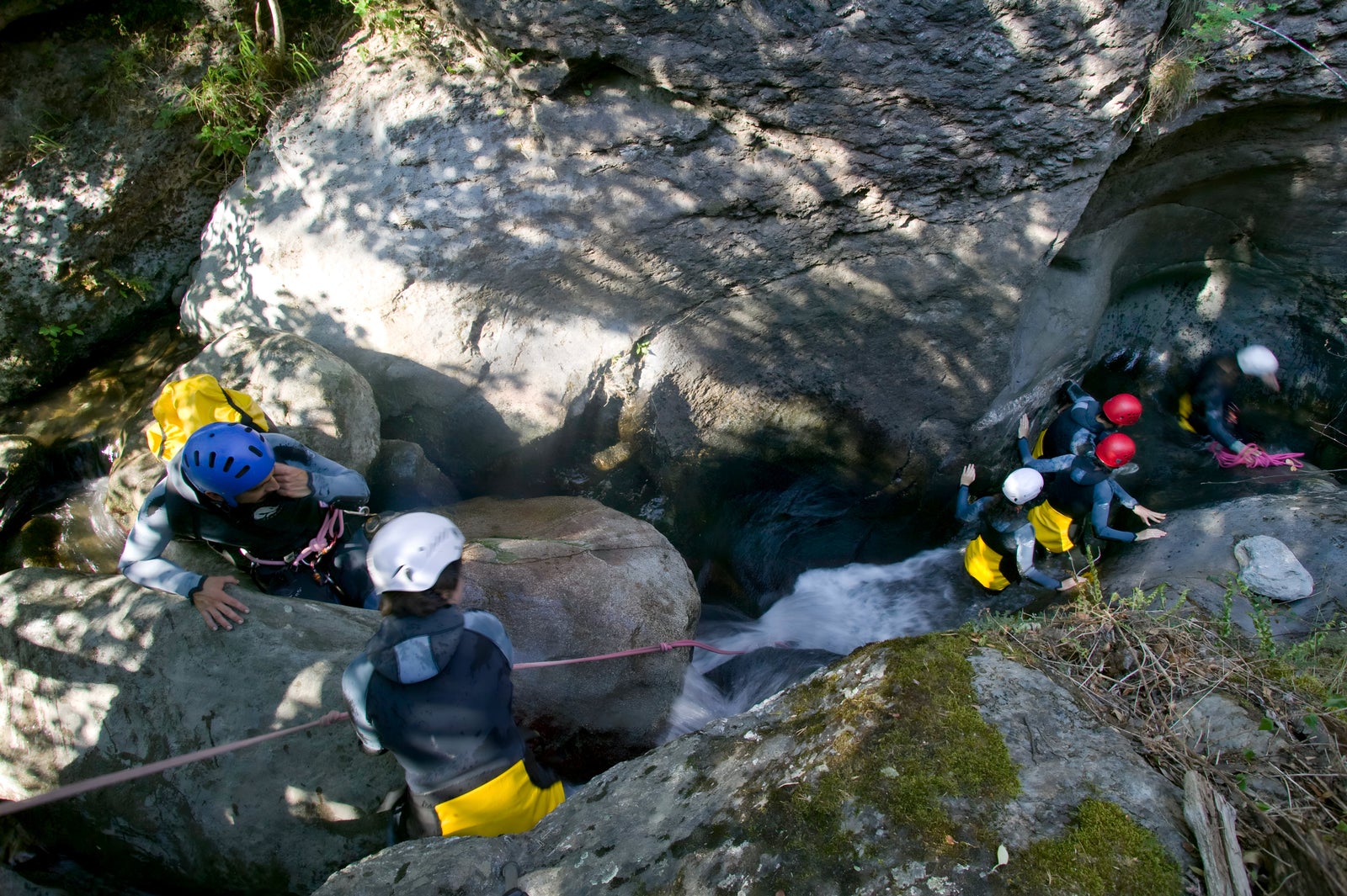 Grupo de personas con cascos y trajes de neopreno practicando barranquismo en un río entre rocas.
