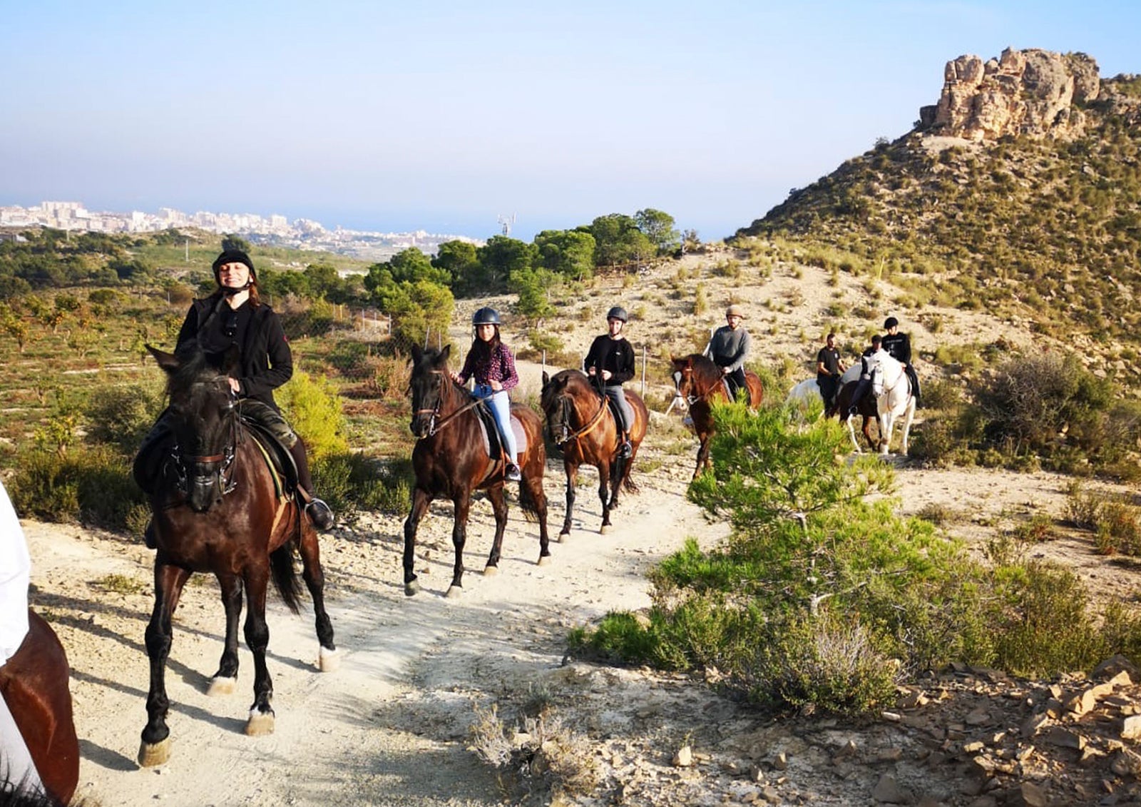 Un grupo de personas realizando una ruta a caballo por un sendero natural en la montaña bajo un cielo despejado.